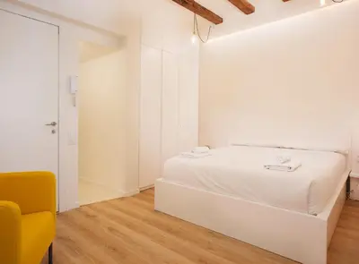 a white bedroom with a bed and a yellow chair at Alsina · Historical center - Barrio Gótico in Barcelona