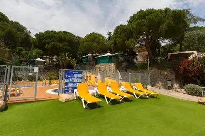 a group of chairs sitting on the grass near a pool at Camping Bungalows El Far in Calella
