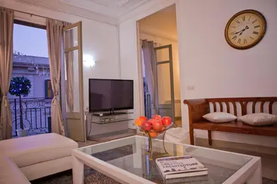 a living room with a table and a clock on the wall at Balcones y Vistas en el Centro de la Ciudad in Barcelona