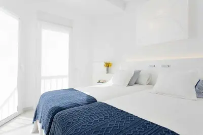 a white bedroom with a large bed with a blue blanket at Sitges Bellavista · Vistas Espectaculares del Mar in Sitges