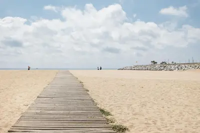 a wooden path on a sandy beach with people in the distance at Matarolux 14 in Mataró