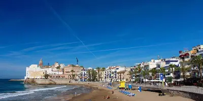 a beach with buildings and people sitting on the beach at Sitges Holiday Apartment in Sitges