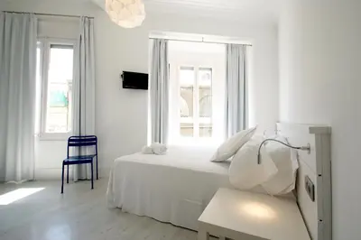 a white bedroom with a bed and a blue chair at Express by gaiarooms in Barcelona