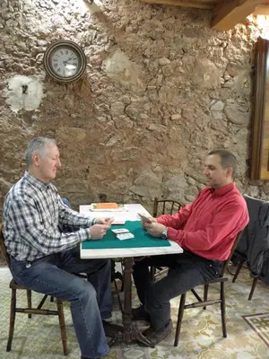 two men sitting at a table in front of a stone wall at Hostal Cal Pla in Sant Llorenc Savall