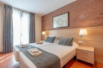 a hotel room with two beds and a brick wall at Serennia Cest Apartamentos Arc de Triomf in Barcelona