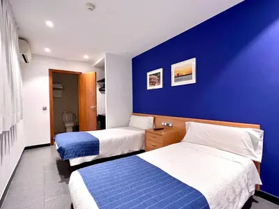 a hotel room with two beds and a blue wall at Hostal Apolo in Barcelona