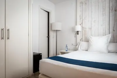 a bedroom with a white bed with a blue stripe at Hotel Medium Sitges Park in Sitges