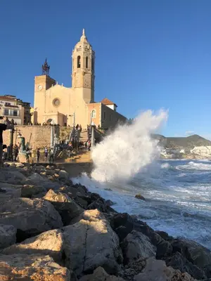 a wave crashes on the beach in front of a church at Apartamento Montroig 3 Ático in Sitges