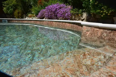 a swimming pool with a stone wall and purple flowers at ARTS HOUSE - Cabrils, Maresme, Barcelona in Cabrils
