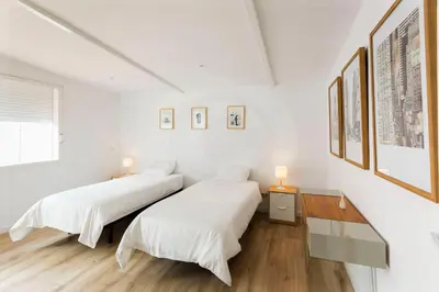 two beds in a room with white walls and wood floors at Antonio's House in Sitges