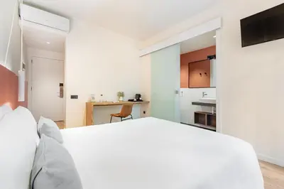 a bedroom with a white bed and a kitchen at LeMar by Aspasios in Barcelona