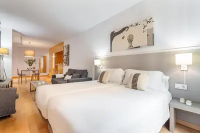 a bedroom with a large white bed and a living room at Aspasios Plaza Real Apartments in Barcelona