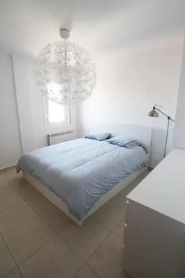 a white bedroom with a bed and a chandelier at Espectacular ático dúplex con vistas al mar in Cunit