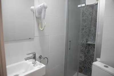 a white bathroom with a shower and a sink at Hostal Ruta de Francia in Barcelona