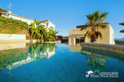 a swimming pool with blue water in front of a house at Stunning Villa Ibizenca with private pool in Sitges in Sitges