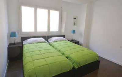 a green bed in a bedroom with two windows at Duplex en frente de la playa al lado de Barcelona in Canet de Mar