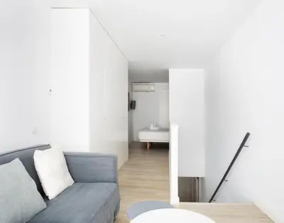 a living room with a gray couch and a bathroom at Urban Suites Sitges Apartments by PriorityVillas in Sitges