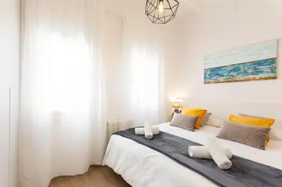a white bedroom with two beds and a chandelier at Confort apartamentos en playa, 3 DRM in Barcelona