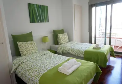 a bedroom with two beds with green sheets and a window at Happy Holiday Beach Home in Sitges