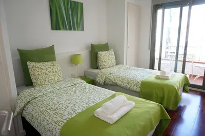 a bedroom with two beds with green sheets and a window at Happy Holiday Beach Home in Sitges