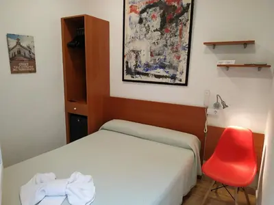 a small bedroom with a bed and a red chair at Hotel Mitus in Canet de Mar