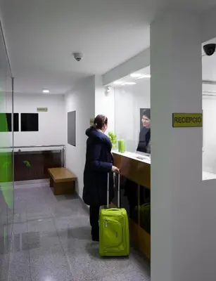 a woman with a green suitcase in an office at Abarco Apartments in Santa Coloma