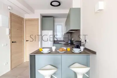 a kitchen with a counter with two white stools at Sitges CENTRAL - En el corazón de Sitges in Sitges