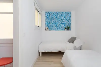 a white bedroom with two beds and a red chair at Casa Cosi - Eixample 3 in Barcelona