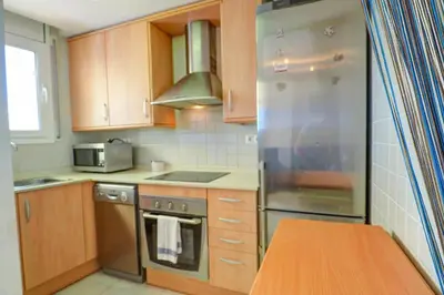 a kitchen with wooden cabinets and a stainless steel refrigerator at Portman Duplex by Hello Homes Sitges in Sitges
