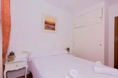 a white bedroom with a bed and a mirror at HomeHolidaysRentals Aube in Sant Cebrià de Vallalta