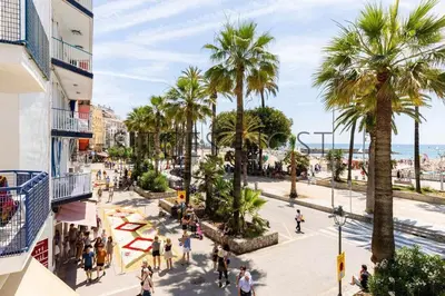 a group of people walking on a street with palm trees at A 20 metros de la playa in Sitges