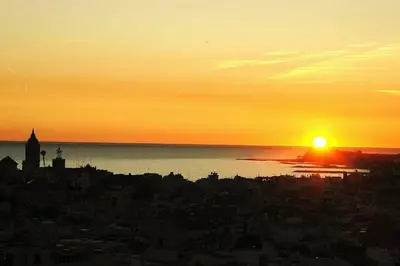 a sunset over a city with the sun setting over the water at APARTAMENTO MARINERO, Vistas impresionantes. in Sitges