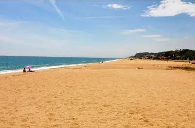a beach with people sitting under an umbrella at Apartamento Pineda in Pineda de Mar