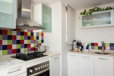 a kitchen with white cabinets and colorful tiles on the wall at Sunny Apartments in Sitges