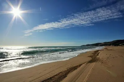 a beach with the sun in the sky and the ocean at Apartaments Maritim in Castelldefels