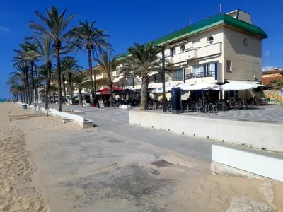 a building on the beach with palm trees and chairs at APARTAMENTO EN SEGUNDA LINEA DE MAR, WIFI & A.C in Cubelles