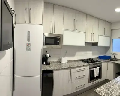 a kitchen with white cabinets and a refrigerator at Amplio Apartamento cerca de FIRA y del Centro in Hospitalet de Llobregat