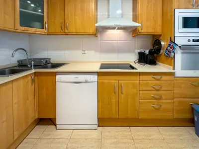 a kitchen with wooden cabinets and a white dishwasher at Sunlight by Hello Homes Sitges in Sitges