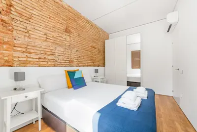 a bedroom with a white bed and a brick wall at Sant Pau Ramblas Apartments Serennia in Barcelona
