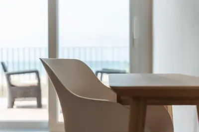a table and a white chair next to a window at Beach Villa Cristina by HHBCN in Castelldefels