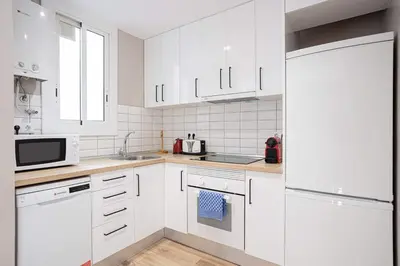 a white kitchen with white cabinets and a refrigerator at Walk To Las Ramblas Sun-filled&cozy in Barcelona