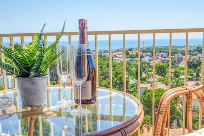 a glass table with wine bottles and glasses on a balcony at Palma Fiesta Apartment by Hello Homes Sitges in Sant Pere de Ribes