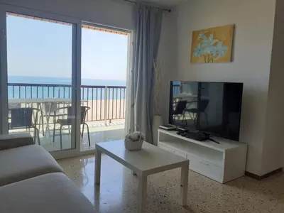 a living room with a couch and a tv and a balcony at Suitur apartamento primera linea mar vistas playa in Canet de Mar