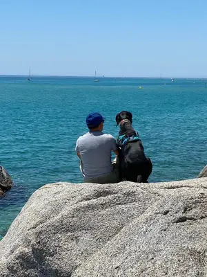 a man and a dog sitting on a rock near the water at Beautiful apartment 5 minutes walk to the beach in Caldes d'Estrac
