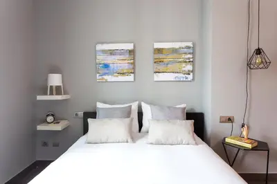 a bedroom with a white bed with three paintings on the wall at Bo&Co Apartments in Sitges