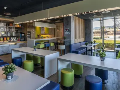 a restaurant with white tables and colorful stools at Ibis Budget Barcelona Viladecans in Viladecáns