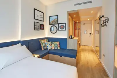 a hotel room with a bed and a blue bench at Hampton By Hilton Barcelona Fira Gran Via in Hospitalet de Llobregat