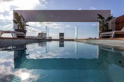 a swimming pool with chairs and the reflection in the water at Art Apartments BCN in Castelldefels