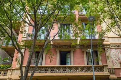 a pink building with a balcony and trees at ApartEasy - Casanova Elegance in Barcelona