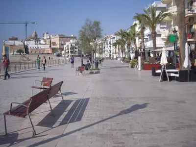 a city street with benches and palm trees and buildings at APARTAMENTO CON OFICINA Y VISTAS AL MAR in Sitges